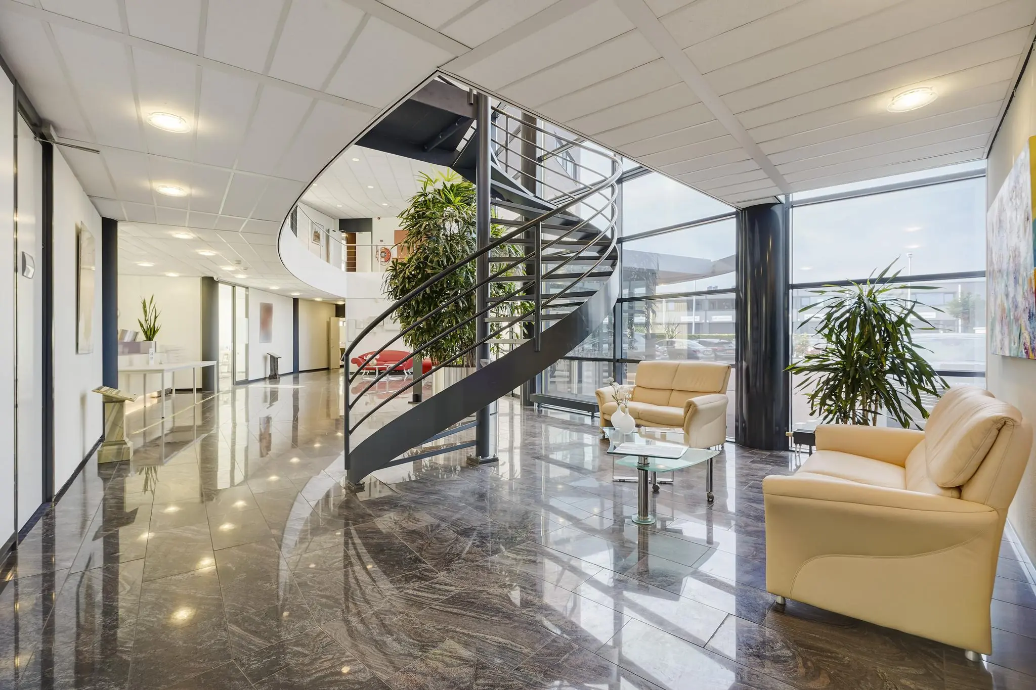 Moderne entreehal van een kantoorpand aan de Laan van ’s-Gravenmade met een glazen gevel, wenteltrap en zithoek met leren banken.